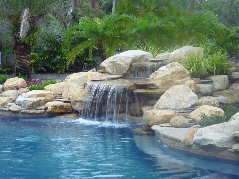 Design ideas for a mid-sized traditional backyard custom-shaped lap pool in Miami with a water feature and natural stone pavers.