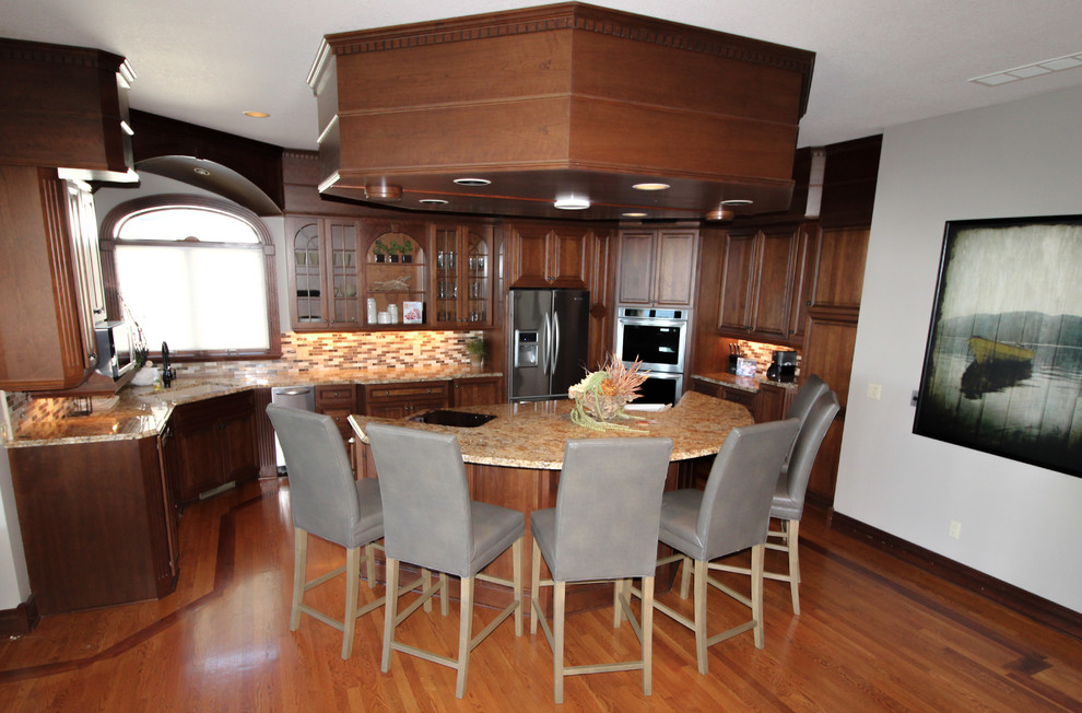 Medium tone wood floor and brown floor kitchen photo with an undermount sink, raised-panel cabinets, dark wood cabinets, granite countertops, multicolored backsplash, ceramic backsplash, stainless steel appliances, an island and orange countertops