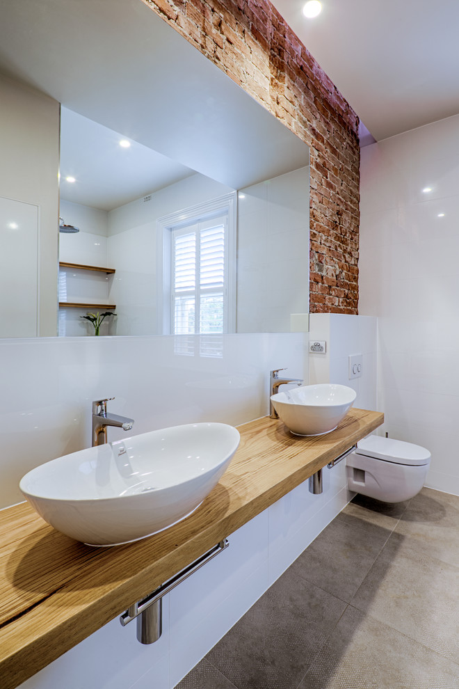 This is an example of a large industrial 3/4 bathroom in Adelaide with furniture-like cabinets, a freestanding tub, gray tile, porcelain tile, white walls, porcelain floors, wood benchtops, distressed cabinets, an open shower, a one-piece toilet, a wall-mount sink, grey floor and brown benchtops.