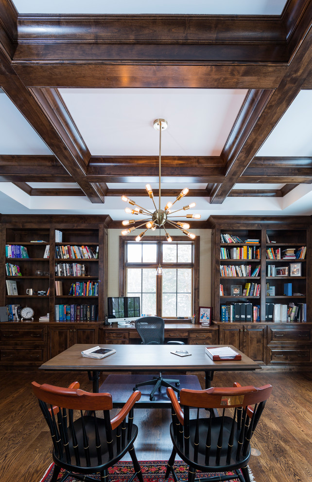 Photo of an arts and crafts home office in Milwaukee with a library, grey walls, dark hardwood floors, a corner fireplace and a freestanding desk.