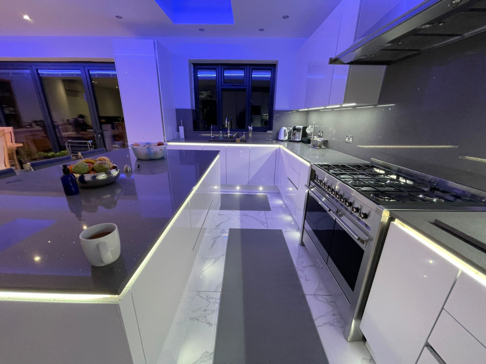 This is an example of a mid-sized modern u-shaped open plan kitchen in London with an integrated sink, flat-panel cabinets, white cabinets, quartzite benchtops, grey splashback, stone slab splashback, stainless steel appliances, porcelain floors, with island, multi-coloured floor and grey benchtop.