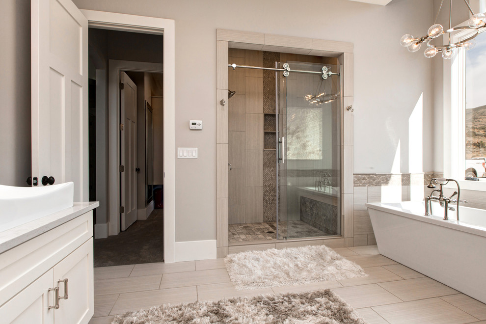This is an example of a large contemporary master bathroom in Salt Lake City with shaker cabinets, white cabinets, a freestanding tub, an alcove shower, beige walls, porcelain floors, a vessel sink, quartzite benchtops, a two-piece toilet, gray tile and stone slab.