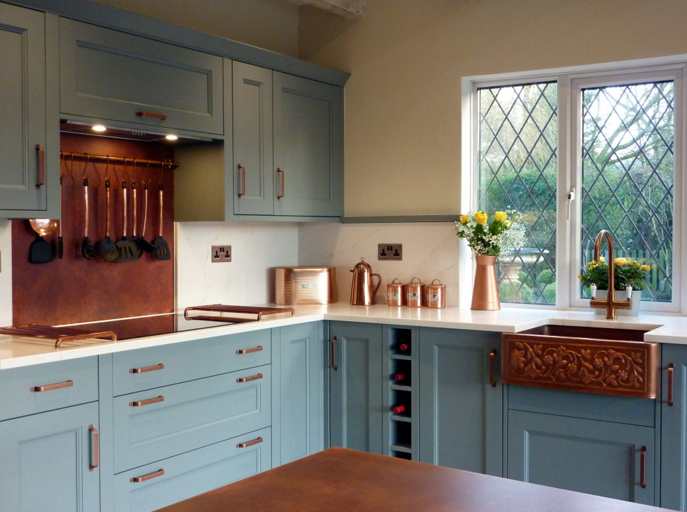 Large traditional galley kitchen/diner in West Midlands with a belfast sink, beaded cabinets, blue cabinets, quartz worktops, orange splashback, black appliances, vinyl flooring, an island, grey floors, white worktops and exposed beams.