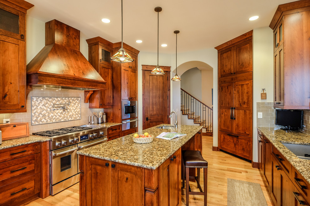 Photo of a large arts and crafts galley separate kitchen in Denver with an undermount sink, shaker cabinets, medium wood cabinets, granite benchtops, brown splashback, subway tile splashback, stainless steel appliances, light hardwood floors and with island.