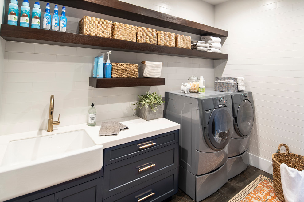 This is an example of a mid-sized transitional galley dedicated laundry room in Los Angeles with an undermount sink, shaker cabinets, blue cabinets, solid surface benchtops, white walls, concrete floors, a side-by-side washer and dryer, grey floor and white benchtop.