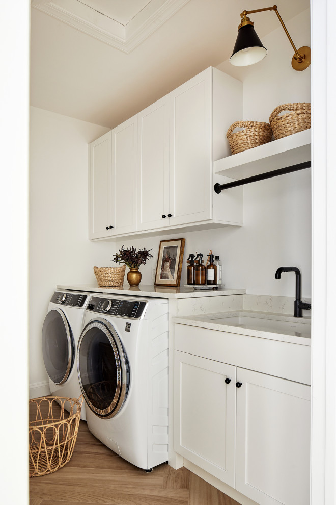 Photo of a medium sized traditional single-wall utility room in Chicago with a submerged sink, recessed-panel cabinets, white cabinets, engineered stone countertops, white splashback, engineered quartz splashback, white walls, porcelain flooring, a side by side washer and dryer, brown floors and white worktops.