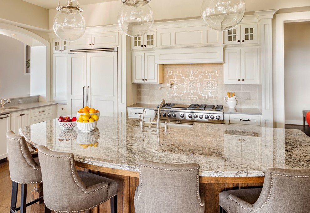 Example of a transitional l-shaped medium tone wood floor kitchen design in Miami with a farmhouse sink, recessed-panel cabinets, white cabinets, granite countertops, beige backsplash, stainless steel appliances and an island
