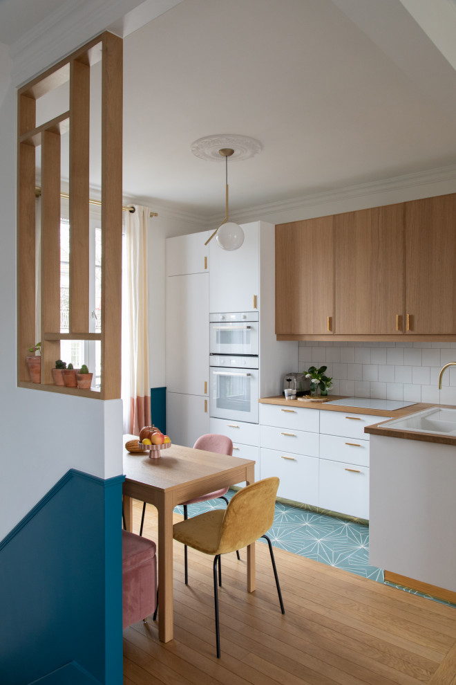Mid-sized modern l-shaped open plan kitchen in Paris with a single-bowl sink, beaded inset cabinets, light wood cabinets, wood benchtops, white splashback, ceramic splashback, white appliances, cement tiles, no island, blue floor and beige benchtop.
