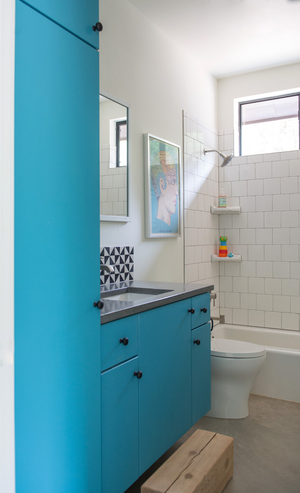 Design ideas for a mid-sized country 3/4 bathroom in Austin with flat-panel cabinets, blue cabinets, an alcove tub, a shower/bathtub combo, a one-piece toilet, white tile, porcelain tile, white walls, concrete floors, an undermount sink and concrete benchtops.