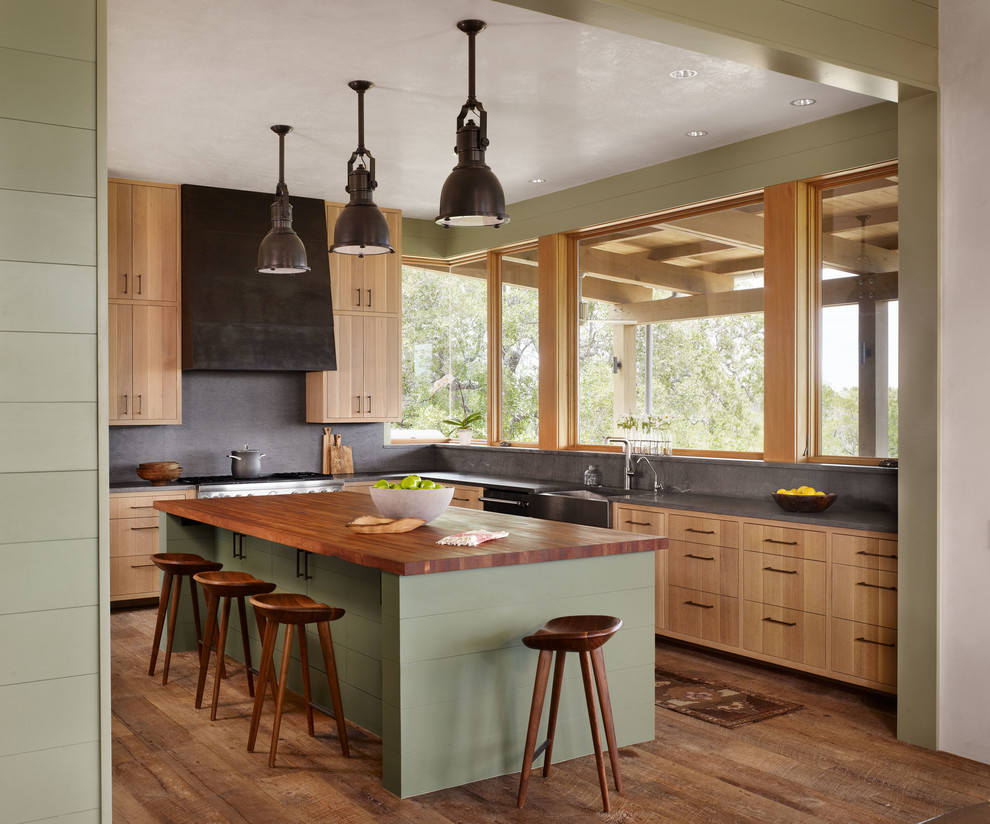 Enclosed kitchen - farmhouse l-shaped medium tone wood floor and brown floor enclosed kitchen idea in Austin with a farmhouse sink, flat-panel cabinets, light wood cabinets, gray backsplash, stone slab backsplash, stainless steel appliances and an island