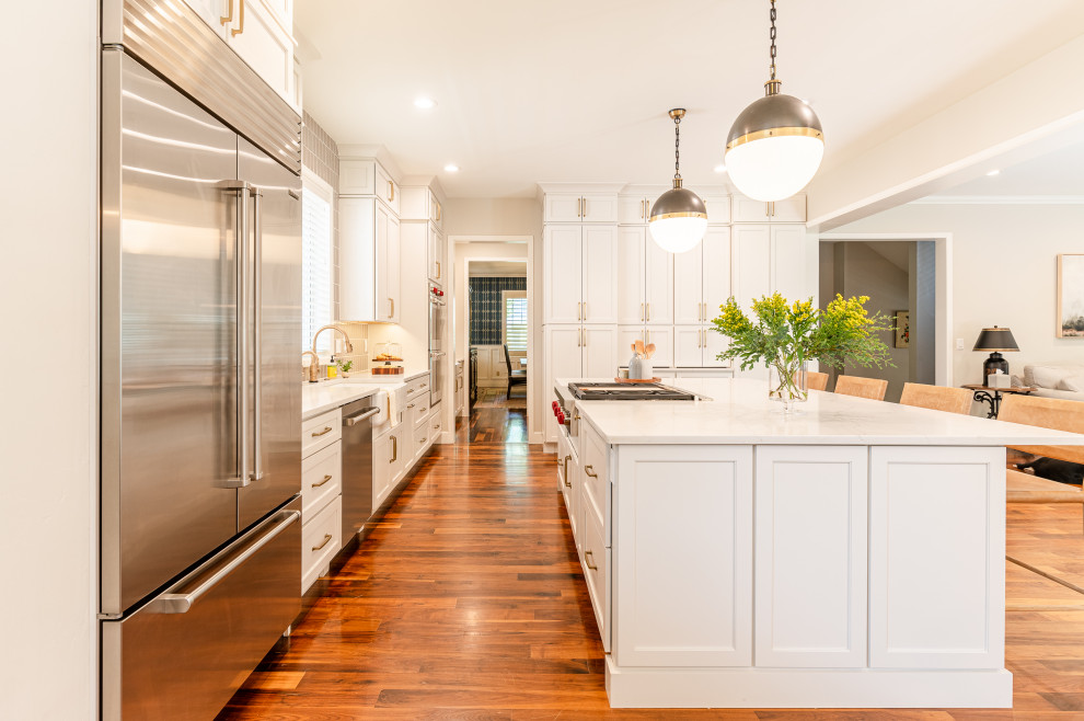 Example of a large transitional l-shaped dark wood floor and brown floor open concept kitchen design in Denver with a farmhouse sink, shaker cabinets, beige cabinets, quartz countertops, beige backsplash, ceramic backsplash, stainless steel appliances, an island and white countertops
