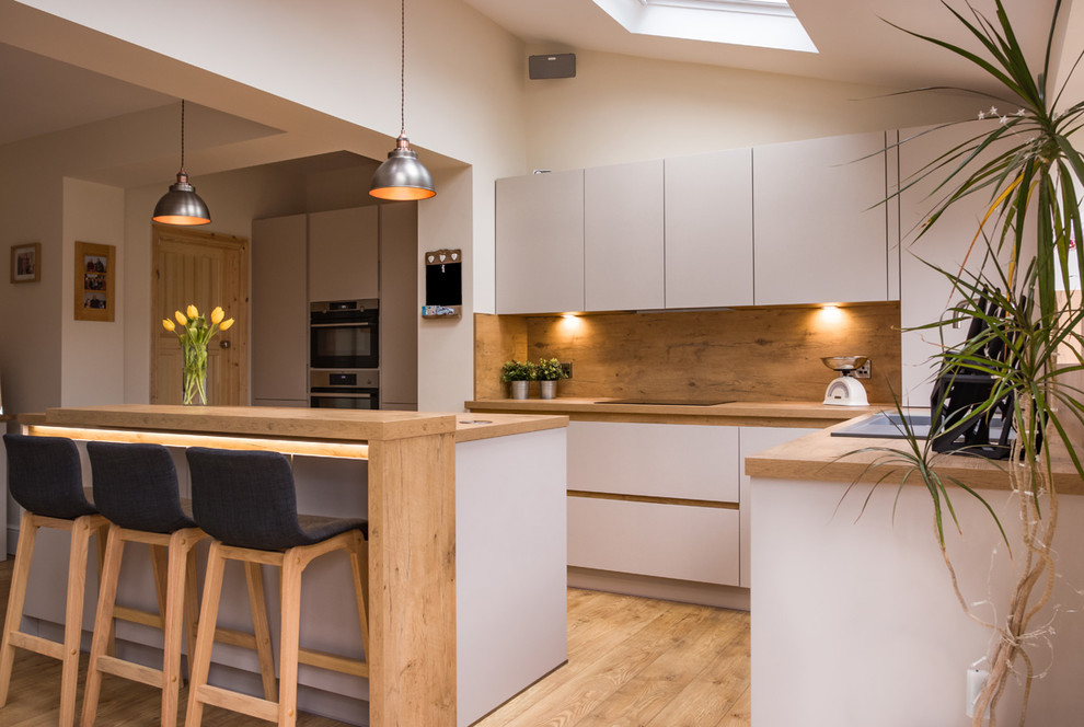 Photo of a mid-sized contemporary l-shaped kitchen in Other with flat-panel cabinets, grey cabinets, wood benchtops, beige splashback, timber splashback, stainless steel appliances, light hardwood floors, with island, brown floor and beige benchtop.