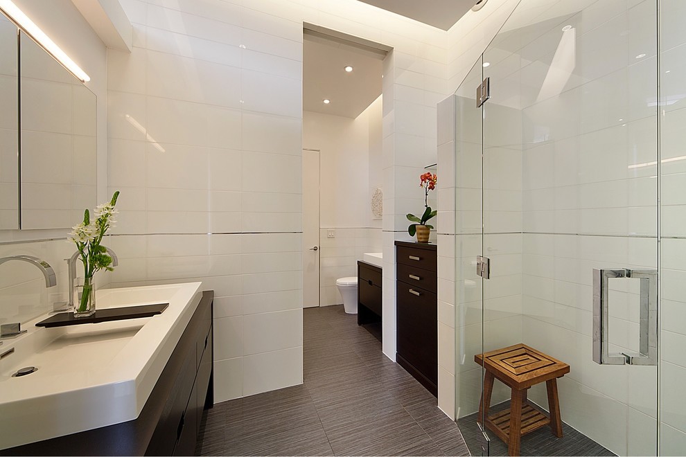 This is an example of a large modern master bathroom in New York with flat-panel cabinets, dark wood cabinets, an alcove shower, white tile, subway tile, white walls, porcelain floors, an integrated sink, brown floor and a hinged shower door.