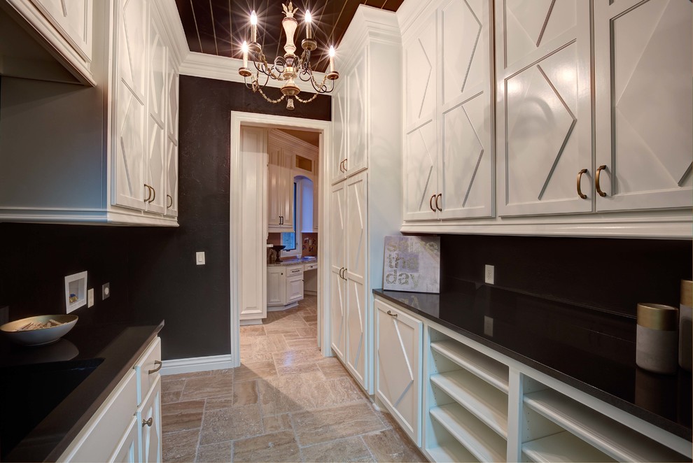 Photo of a large transitional galley dedicated laundry room in Oklahoma City with shaker cabinets, white cabinets, solid surface benchtops, black walls, limestone floors and a side-by-side washer and dryer.