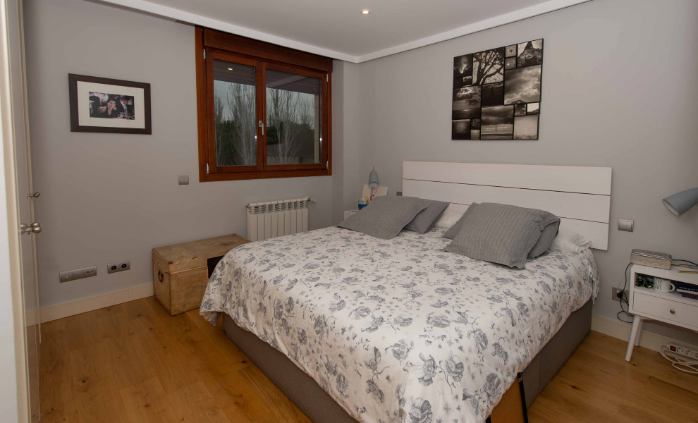 Aménagement d'une chambre parentale grise et blanche moderne de taille moyenne avec un mur gris, un sol en bois brun et un sol marron.
