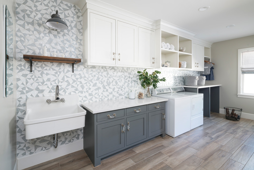 Design ideas for a large country single-wall dedicated laundry room in Phoenix with a farmhouse sink, shaker cabinets, blue cabinets, quartz benchtops, grey walls, ceramic floors, a side-by-side washer and dryer, brown floor and white benchtop.