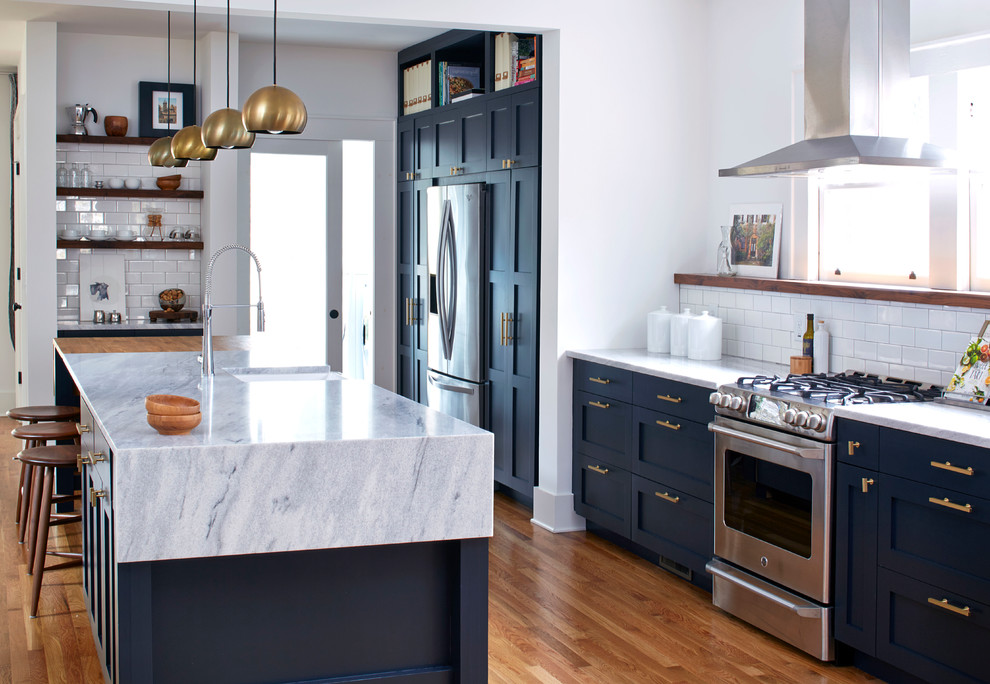 This is an example of a mid-sized transitional galley eat-in kitchen in Atlanta with a farmhouse sink, shaker cabinets, blue cabinets, marble benchtops, white splashback, ceramic splashback, stainless steel appliances, medium hardwood floors, with island and brown floor.