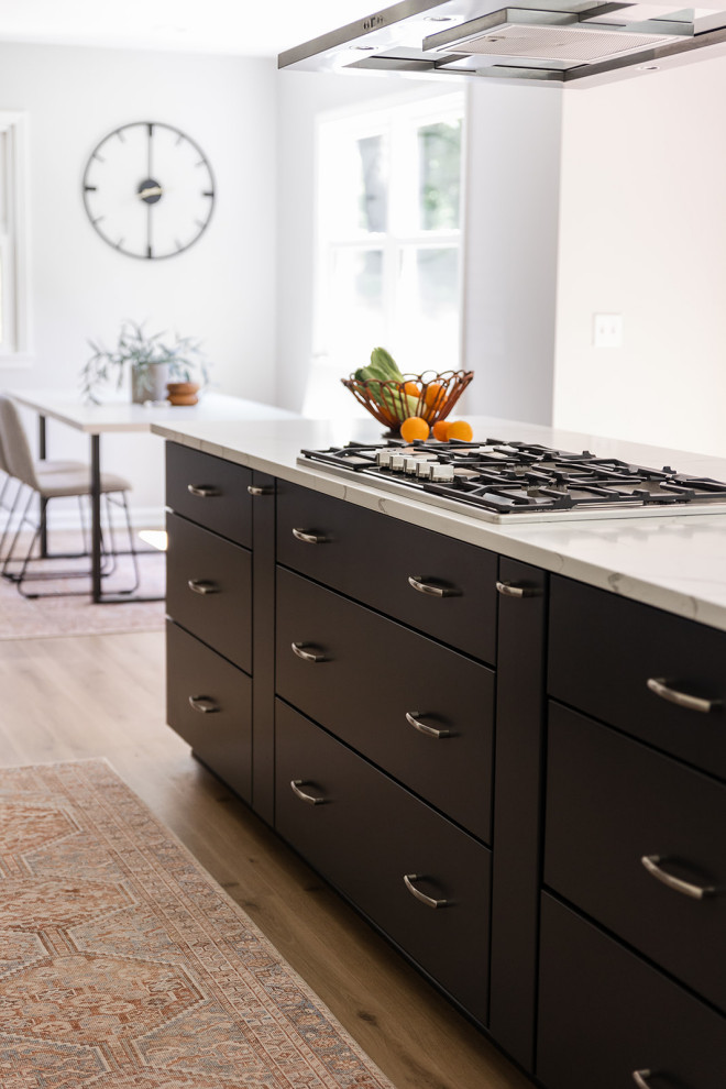Inspiration for a mid-sized transitional galley vinyl floor and brown floor eat-in kitchen remodel with an undermount sink, shaker cabinets, black cabinets, quartz countertops, white backsplash, stainless steel appliances, an island and white countertops