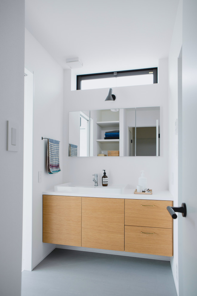 Photo of a mid-sized modern powder room in Other with beaded inset cabinets, light wood cabinets, white tile, porcelain tile, white walls, concrete floors, a drop-in sink, wood benchtops, grey floor, white benchtops, a built-in vanity, wallpaper and wallpaper.