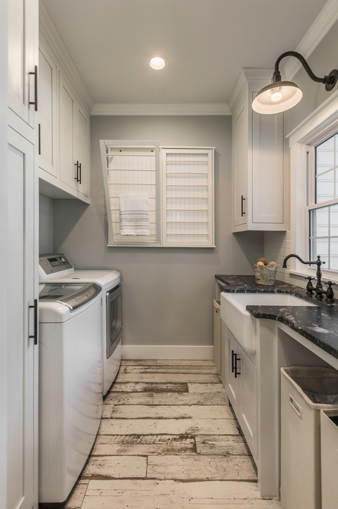 Mid-sized farmhouse galley ceramic tile and beige floor dedicated laundry room photo with a farmhouse sink, flat-panel cabinets, gray cabinets, granite countertops, gray walls, a side-by-side washer/dryer and black countertops