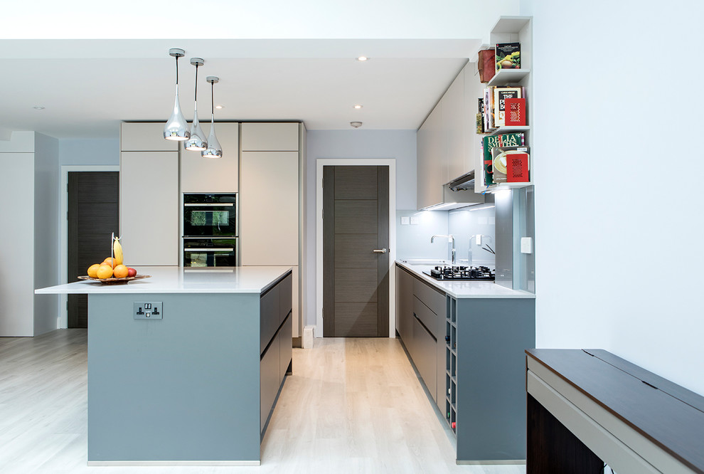 Design ideas for a mid-sized contemporary l-shaped eat-in kitchen in London with blue splashback, with island, an undermount sink, flat-panel cabinets, white benchtop, white cabinets, glass sheet splashback, black appliances, light hardwood floors and beige floor.
