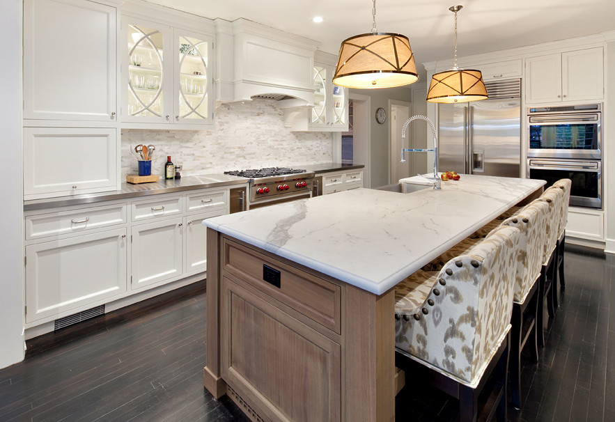 Design ideas for a mid-sized transitional l-shaped open plan kitchen in New York with a farmhouse sink, recessed-panel cabinets, white cabinets, marble benchtops, beige splashback, mosaic tile splashback, stainless steel appliances, dark hardwood floors, with island and brown floor.