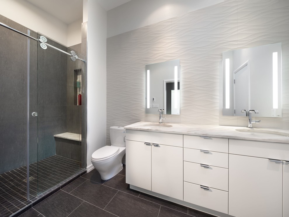 Photo of a contemporary master bathroom in DC Metro with flat-panel cabinets, white cabinets, an alcove shower, a two-piece toilet, gray tile, ceramic tile, white walls, ceramic floors, an undermount sink, marble benchtops, black floor, a sliding shower screen and grey benchtops.