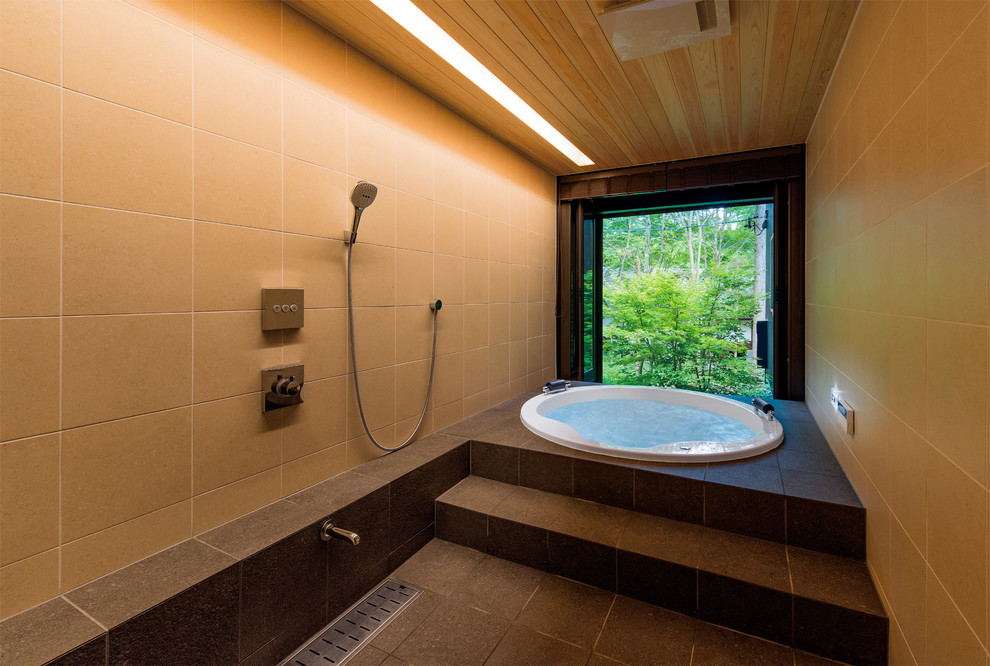Photo of an asian bathroom with a hot tub, beige tile, porcelain tile, beige walls, porcelain floors and black floor.