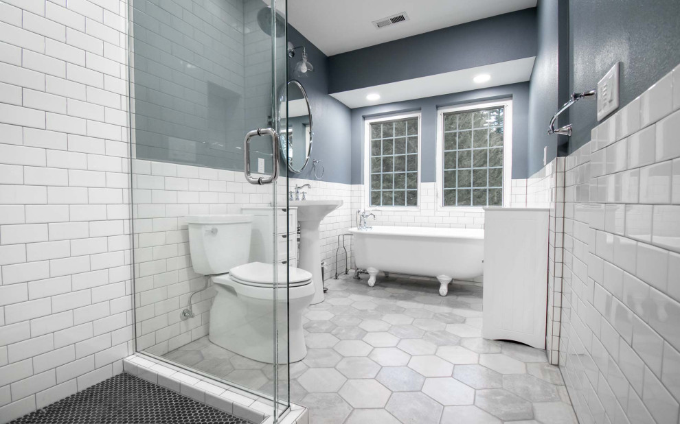 Photo of a mid-sized transitional master bathroom in Portland with a claw-foot tub, a corner shower, a two-piece toilet, white tile, subway tile, blue walls, ceramic floors, a pedestal sink, grey floor, a hinged shower door, a niche and a single vanity.