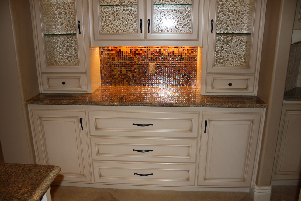 Travertine floor kitchen photo with raised-panel cabinets, distressed cabinets, granite countertops, multicolored backsplash, glass tile backsplash and brown walls