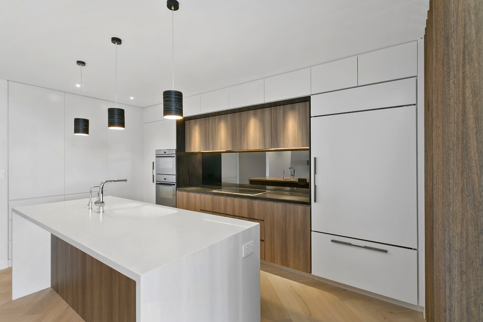 Photo of a mid-sized contemporary l-shaped open plan kitchen in Sydney with an integrated sink, medium wood cabinets, solid surface benchtops, mirror splashback and light hardwood floors.