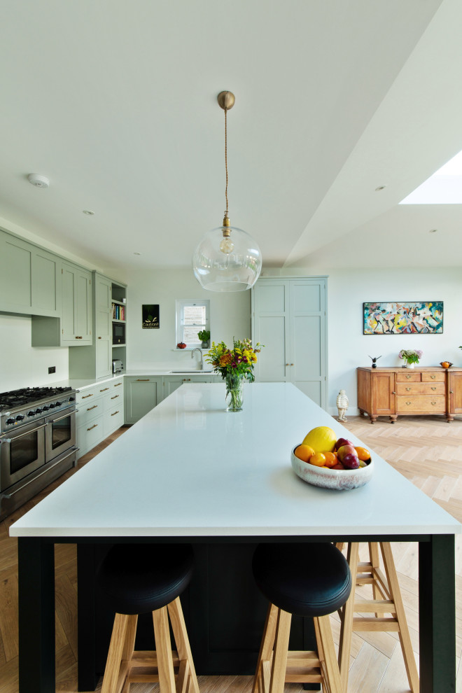 Inspiration for a large transitional u-shaped open plan kitchen in London with an undermount sink, shaker cabinets, green cabinets, quartzite benchtops, white splashback, engineered quartz splashback, stainless steel appliances, medium hardwood floors, with island and white benchtop.