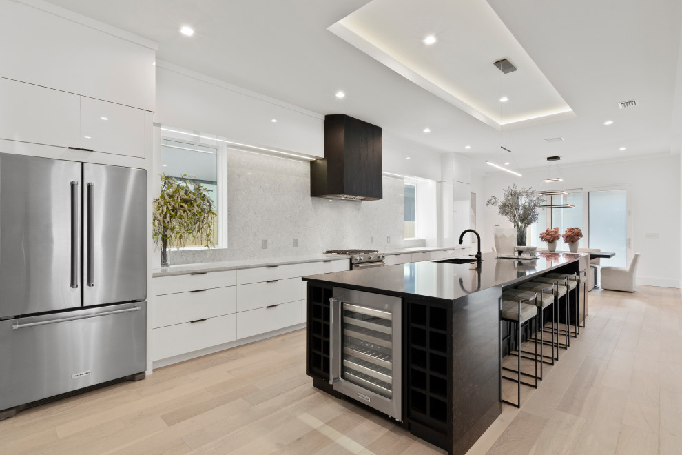 Inspiration for a contemporary galley kitchen in Orlando with an undermount sink, flat-panel cabinets, white cabinets, grey splashback, stainless steel appliances, light hardwood floors, with island, beige floor, black benchtop and recessed.