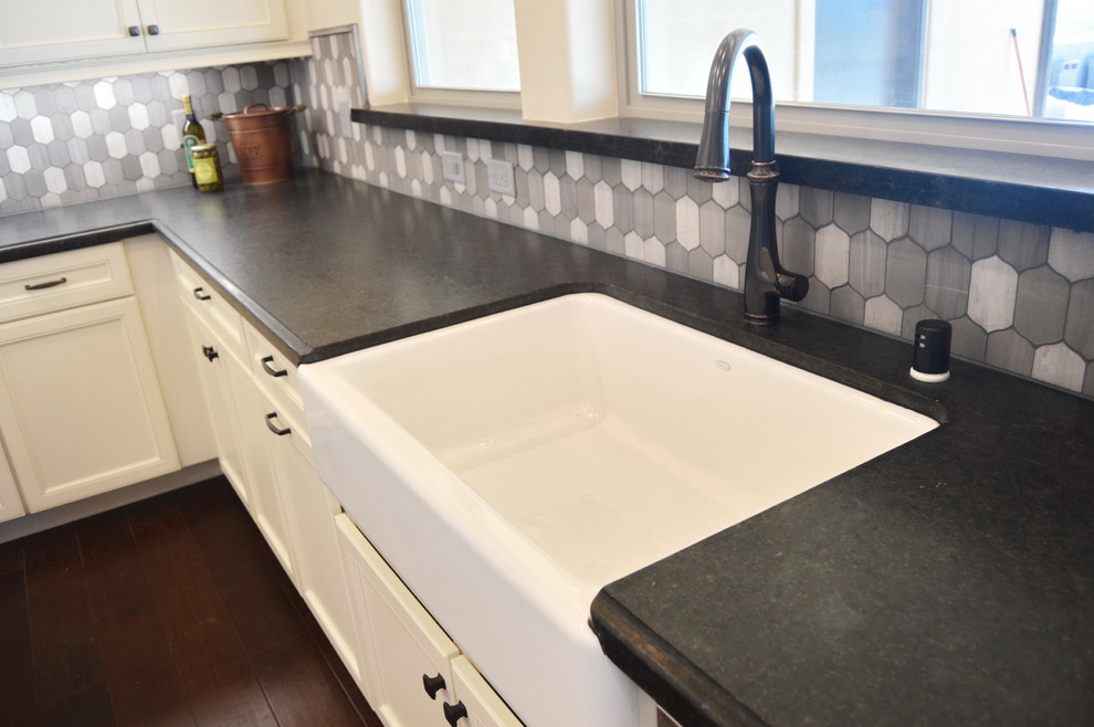 Enclosed kitchen - mid-sized transitional u-shaped medium tone wood floor enclosed kitchen idea with a farmhouse sink, recessed-panel cabinets, white cabinets, solid surface countertops, gray backsplash, ceramic backsplash, stainless steel appliances and an island