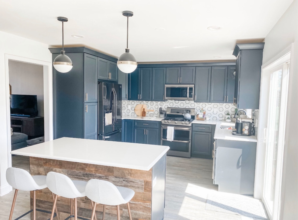 This is an example of a mid-sized country u-shaped eat-in kitchen in Chicago with an undermount sink, shaker cabinets, grey cabinets, quartz benchtops, grey splashback, porcelain splashback, stainless steel appliances, vinyl floors, with island, brown floor and white benchtop.