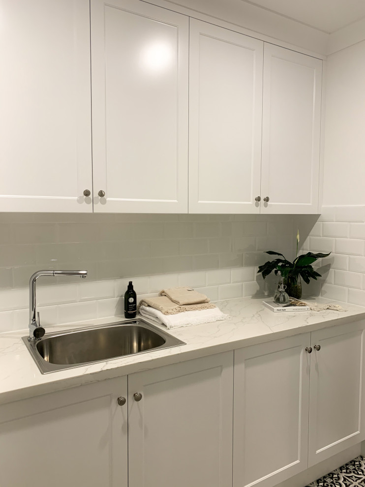 Inspiration for a contemporary galley dedicated laundry room in Brisbane with shaker cabinets, white cabinets, marble benchtops, white splashback, ceramic splashback, ceramic floors, a concealed washer and dryer, multi-coloured floor and white benchtop.