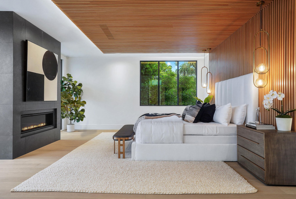 This is an example of a large modern master bedroom in San Diego with white walls, light hardwood floors, a standard fireplace, a tile fireplace surround, brown floor, wood and wood walls.