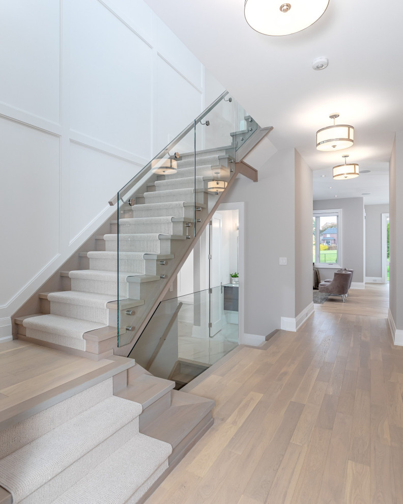 Inspiration for a mid-sized transitional wood u-shaped staircase in Toronto with glass railing, wood risers and panelled walls.