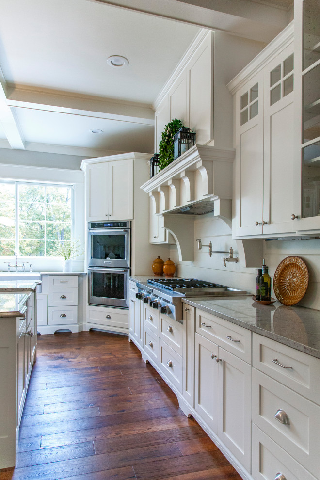 This is an example of a large country u-shaped separate kitchen in Other with a farmhouse sink, shaker cabinets, white cabinets, quartzite benchtops, white splashback, timber splashback, stainless steel appliances, with island, brown floor, grey benchtop and dark hardwood floors.