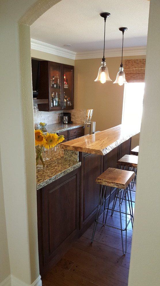 Photo of a country wet bar in San Diego with an undermount sink, glass-front cabinets, dark wood cabinets, wood benchtops, beige splashback, stone tile splashback and medium hardwood floors.
