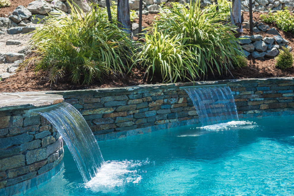 This is an example of a mid-sized tropical backyard kidney-shaped pool in Sacramento with a water feature and natural stone pavers.
