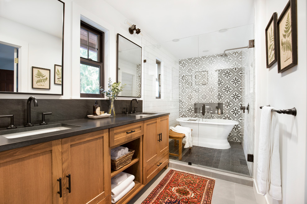 Design ideas for a mid-sized country master wet room bathroom in Seattle with shaker cabinets, medium wood cabinets, a freestanding tub, black and white tile, white walls, an undermount sink, grey floor, a hinged shower door, black benchtops and a double vanity.
