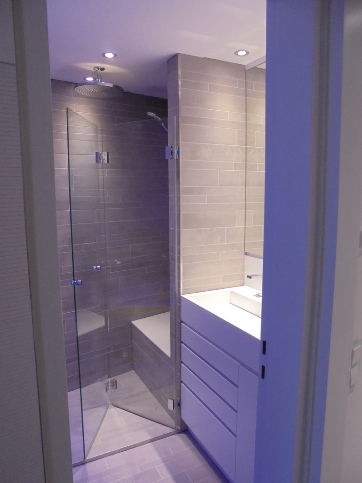 This is an example of a small contemporary 3/4 bathroom in Stuttgart with flat-panel cabinets, white cabinets, an alcove tub, a curbless shower, a wall-mount toilet, gray tile, ceramic tile, grey walls, ceramic floors, an integrated sink, solid surface benchtops, grey floor, a sliding shower screen and white benchtops.