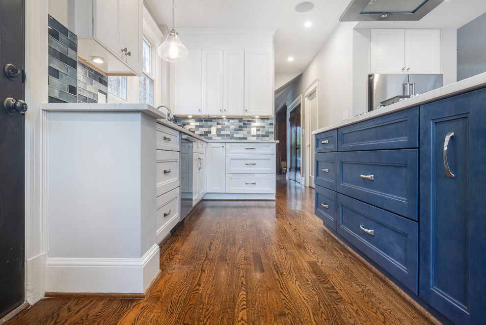 Traditional kitchen in DC Metro with an undermount sink, shaker cabinets, quartz benchtops, blue splashback, glass tile splashback, stainless steel appliances, painted wood floors, with island, brown floor and white benchtop.