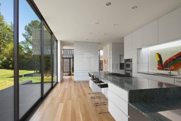 Design ideas for an expansive modern galley separate kitchen in Charlotte with a double-bowl sink, flat-panel cabinets, white cabinets, granite benchtops, glass sheet splashback, panelled appliances, light hardwood floors and with island.
