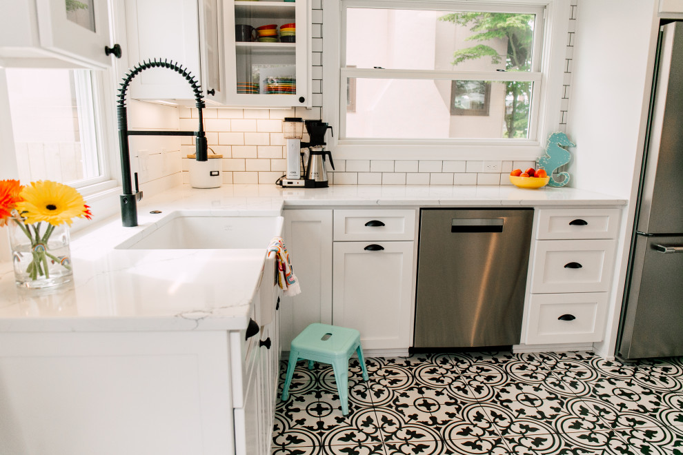 Small eclectic u-shaped separate kitchen in Seattle with a farmhouse sink, shaker cabinets, white cabinets, quartz benchtops, white splashback, ceramic splashback, stainless steel appliances, porcelain floors, no island, black floor and white benchtop.