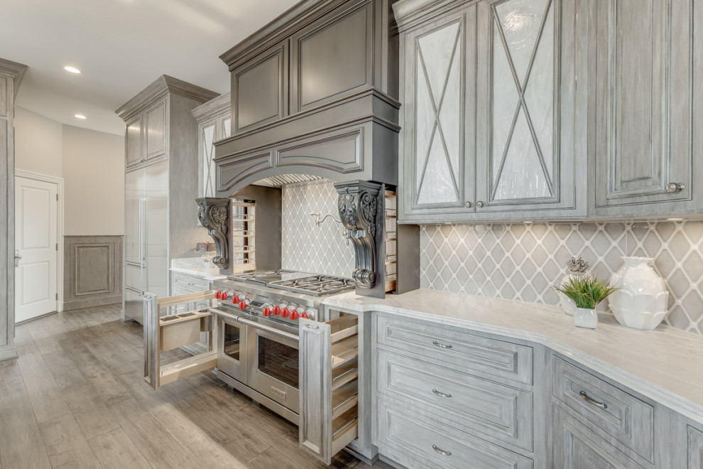 Photo of a large traditional u-shaped open plan kitchen in DC Metro with a farmhouse sink, raised-panel cabinets, distressed cabinets, granite benchtops, beige splashback, ceramic splashback, stainless steel appliances, dark hardwood floors, with island, grey floor and grey benchtop.