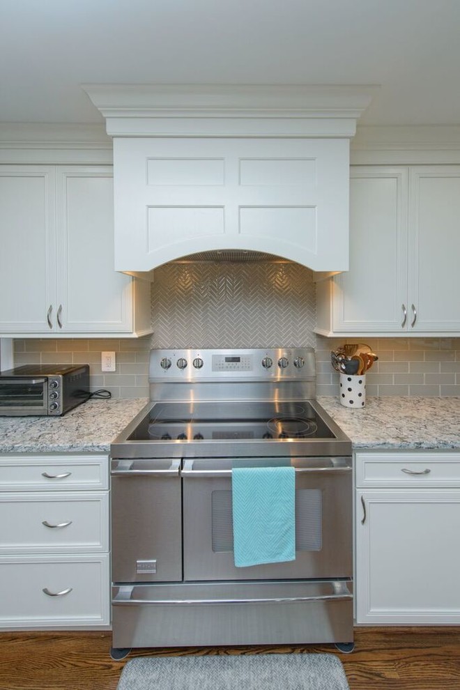 Inspiration for a transitional l-shaped medium tone wood floor eat-in kitchen remodel in Baltimore with a farmhouse sink, beaded inset cabinets, white cabinets, granite countertops, gray backsplash, glass tile backsplash, stainless steel appliances and an island