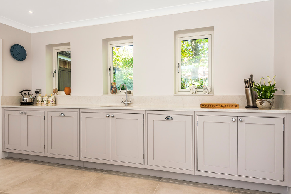 This is an example of a transitional u-shaped eat-in kitchen in Hampshire with an undermount sink, shaker cabinets, grey cabinets, granite benchtops, black appliances, with island, grey floor and grey benchtop.