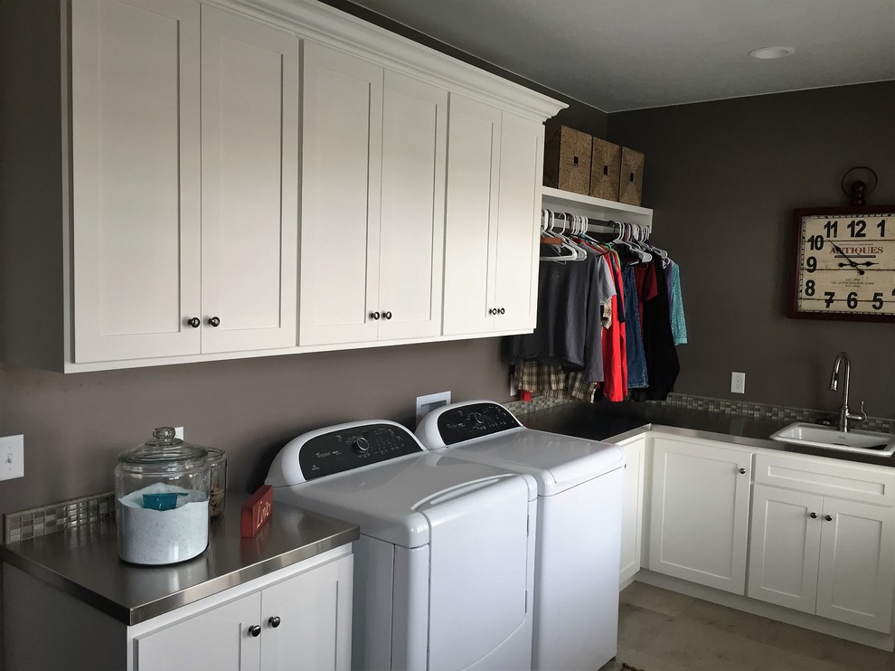 Design ideas for a mid-sized transitional l-shaped utility room in Salt Lake City with a drop-in sink, shaker cabinets, white cabinets, stainless steel benchtops, grey walls, porcelain floors and a side-by-side washer and dryer.